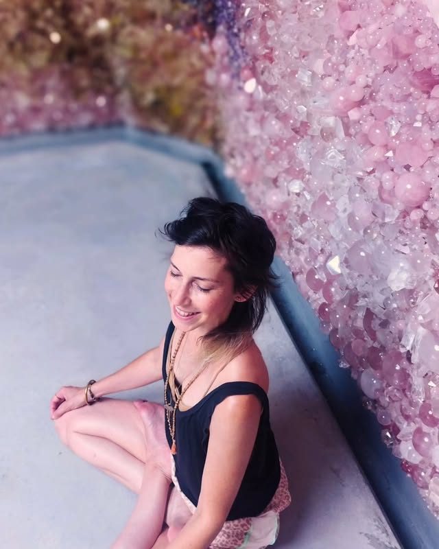 Helen Eastwood seated by a wall of rose-quartz crystals, smiling softly