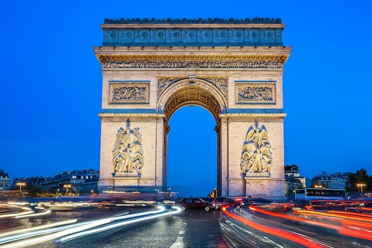 The Arc de Triomphe at night, headlights tracing rivers of light around it