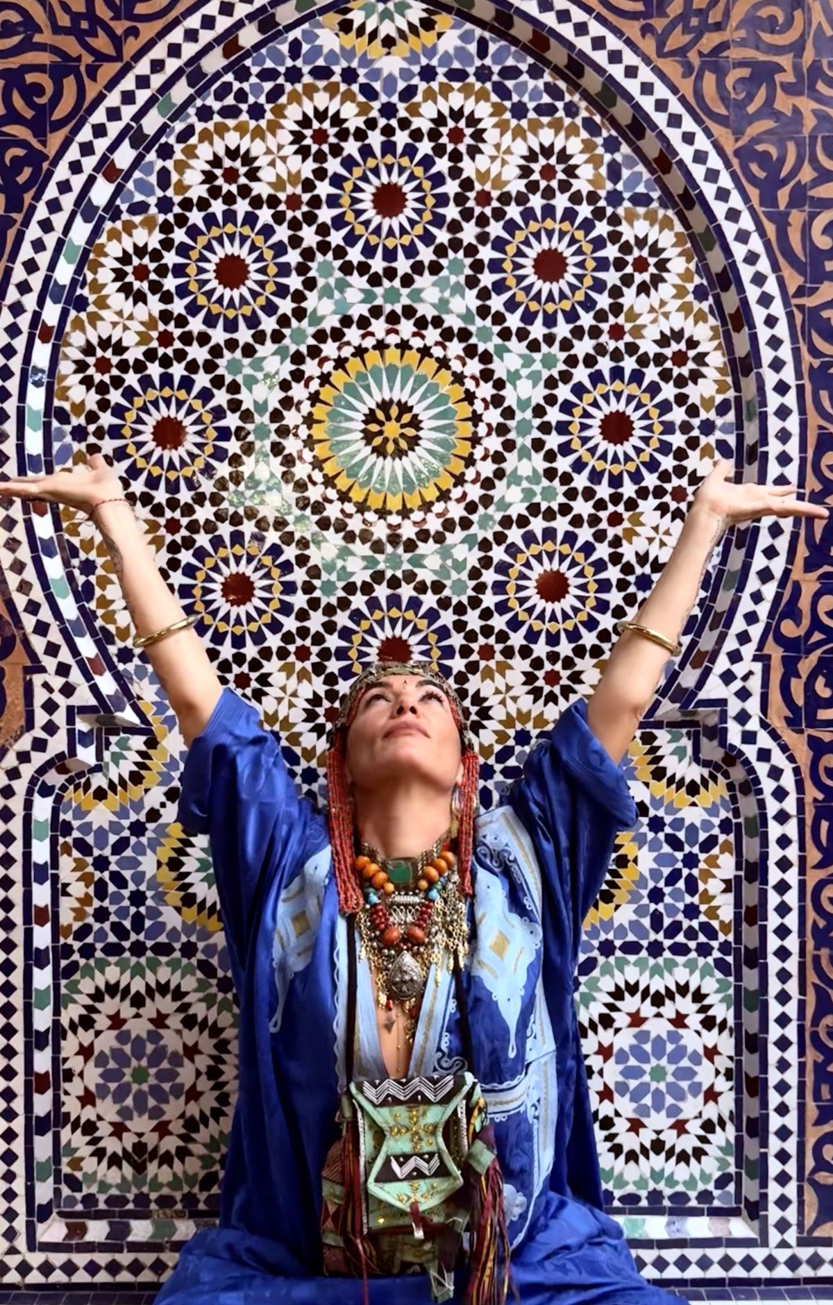 Julia Grant-Scott in front of an intricate Moroccan mosaic, arms raised in devotion